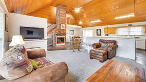 A spacious living area with a fireplace, a television, and a kitchen in the background. - 'deer Lake Lodge' on 700 Wooded Acres in Dayton! (Dayton)