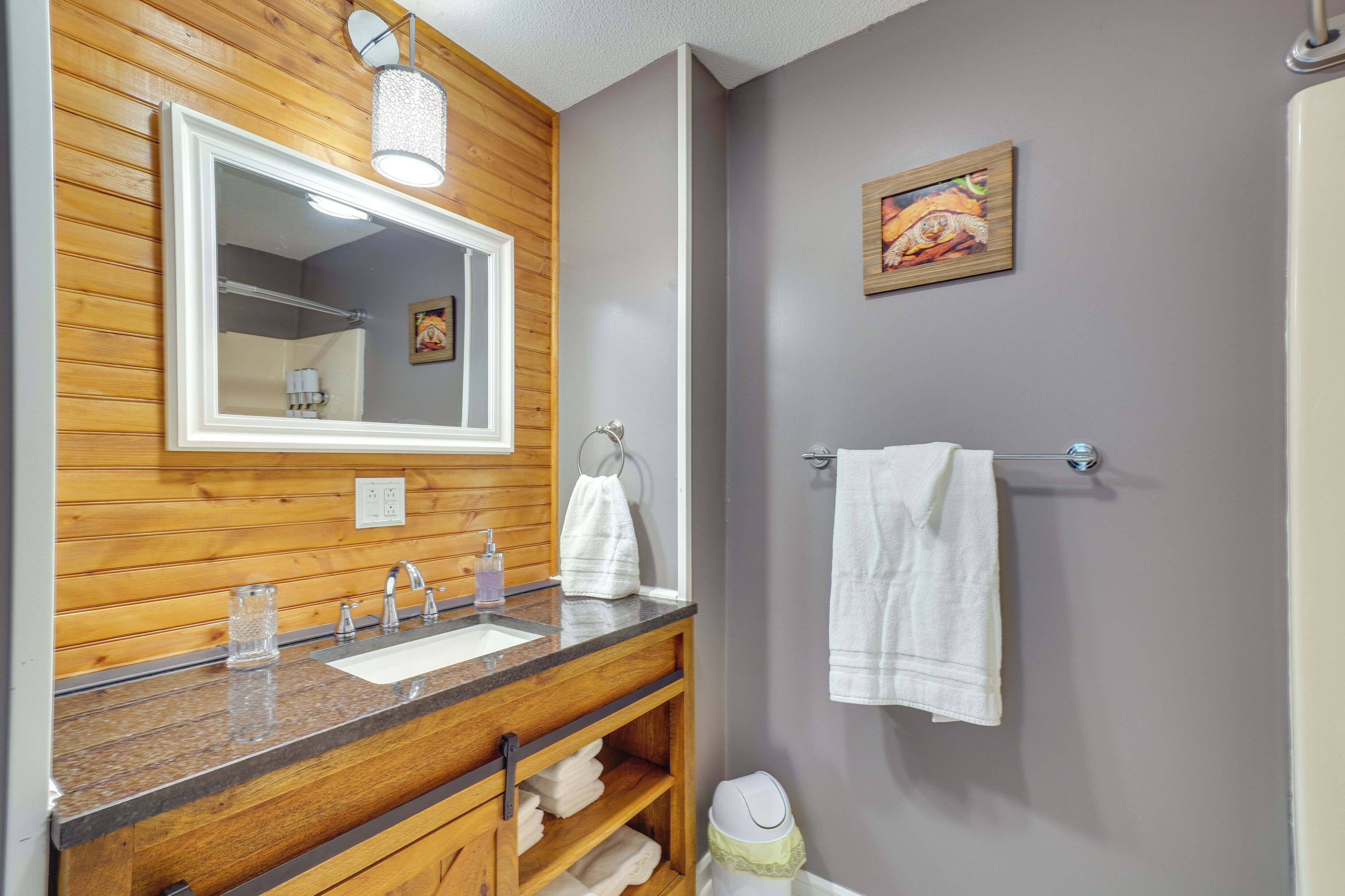 Een badkamer met houten lambrisering, een grote spiegel, een wastafel met een granieten blad, een handdoekrek en een toilet.