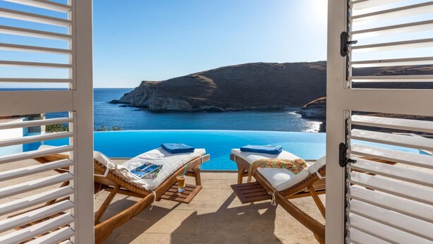 A balcony with two wooden lounge chairs, a small pool, and a view of the sea and a cliff. - Inviting 8-bed Villa in Ermoupoli - Villa Blueros (Syros)