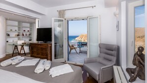 A hotel room with a bed, a desk, a TV, a chair, and a view of the sea. - Inviting 8-bed Villa in Ermoupoli - Villa Blueros (Syros)