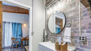 A bathroom with a wooden vanity, a round mirror, and a brick wall.