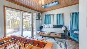 A cozy living room with a foosball table, a sofa, and a bed with blue curtains.