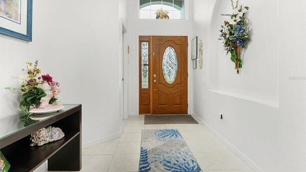 Un couloir avec une porte en bois, une console sur laquelle est posé un vase de fleurs, une plante fixée au mur et un tapis à motifs.