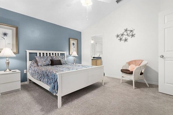 Un dormitorio con cama, mesitas de noche, una silla y un espejo.