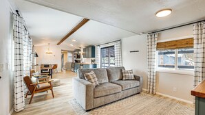 A modern living room with a sofa, a dining area, and a kitchen in the background. - Downtown Cascade Vacation Rental < 1 Mi to Lake! (Cascade)