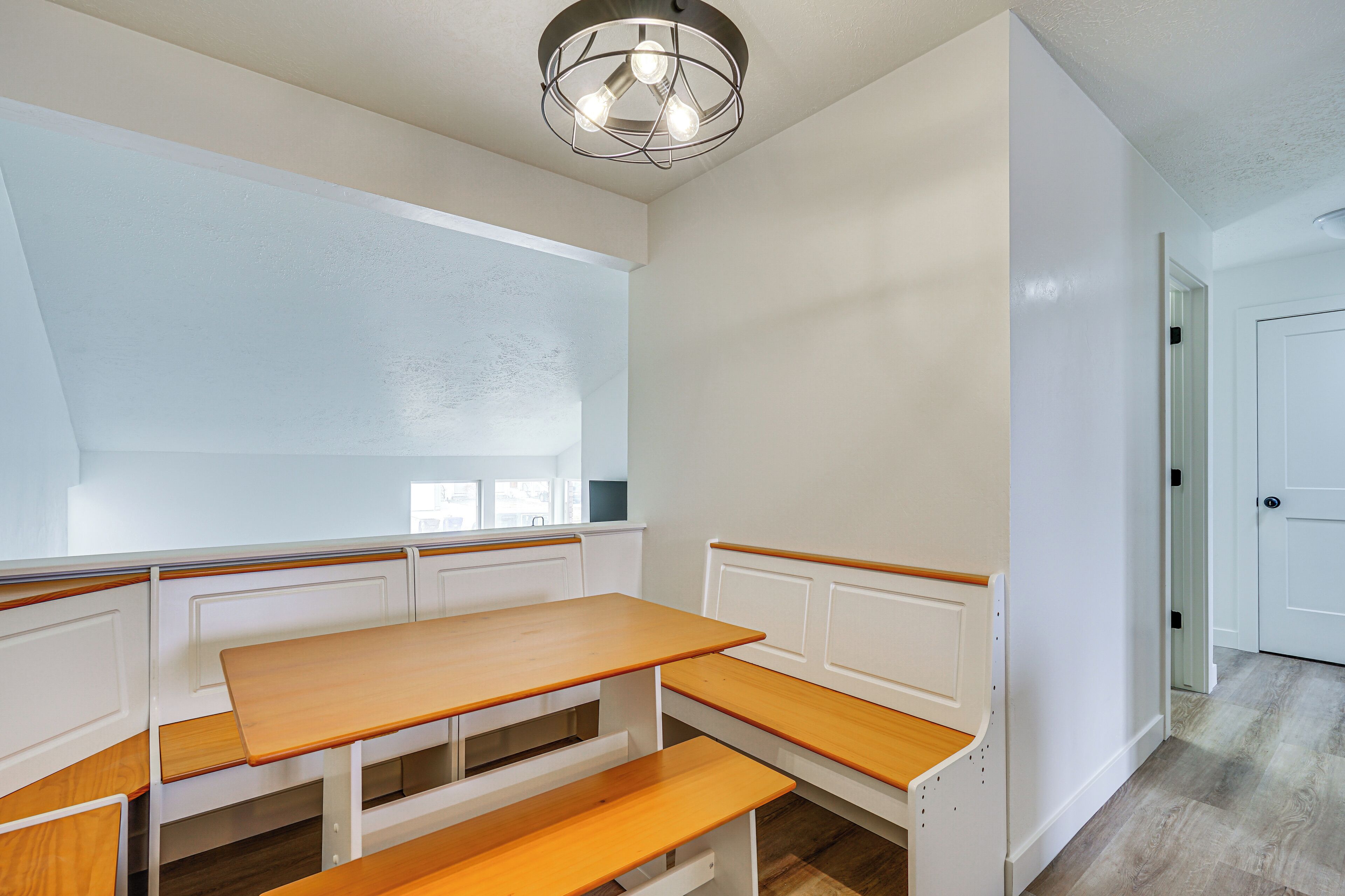 A kitchen with white cabinetry, a wooden bench, and a pendant light.