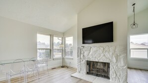 A spacious living room with a stone fireplace, a mounted TV, and large windows offering views of the outside. - Salt Lake County Home Near 4 Major Ski Resorts! (Midvale)
