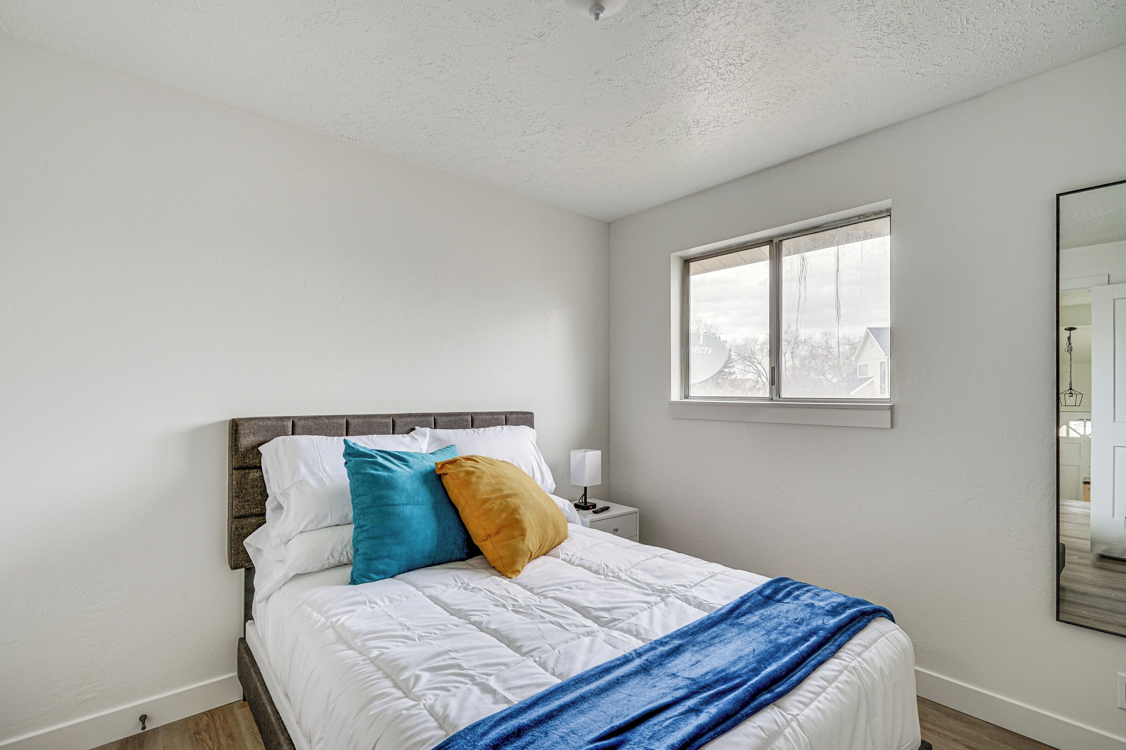 A bedroom with a bed, white walls, a window, and a nightstand with a lamp.