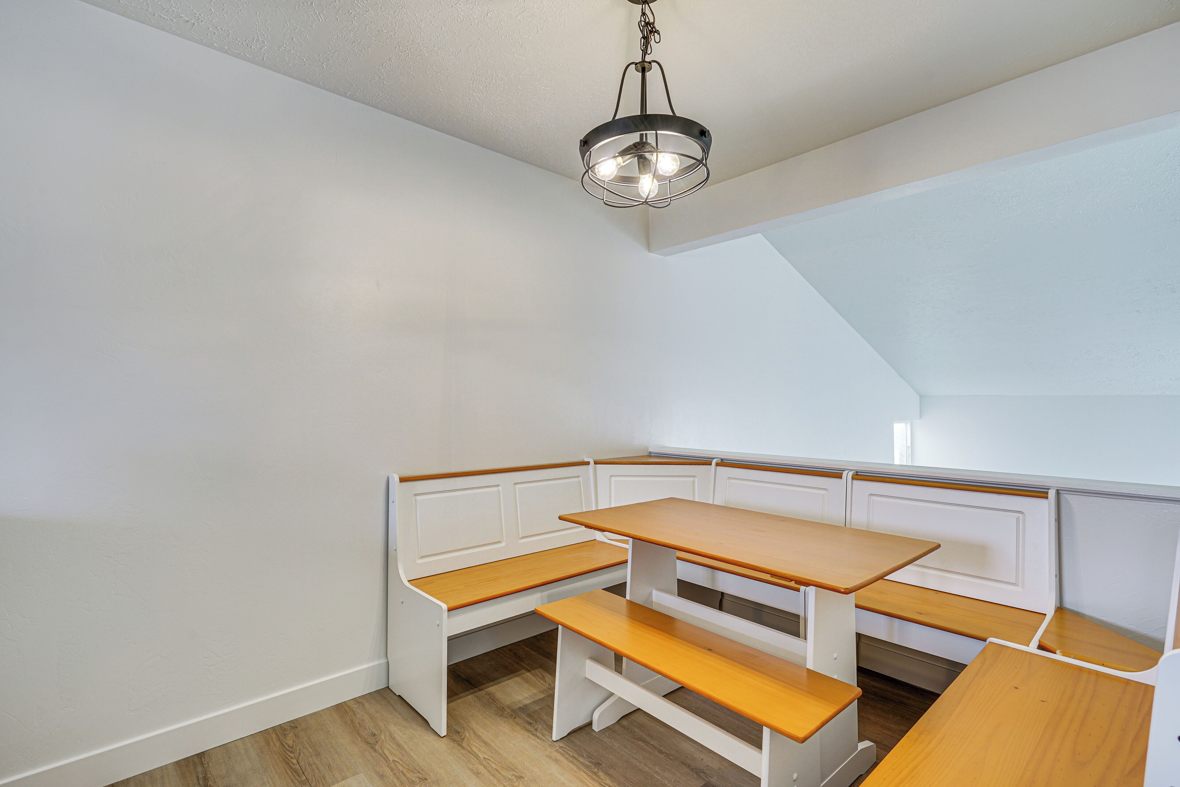 Un'area salotto angolare con una panca e un tavolo, un lampadario a soffitto e un soffitto spiovente.