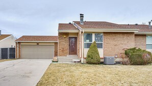 A two-story house with a garage, a chimney, and a well-maintained lawn. - Salt Lake County Home Near 4 Major Ski Resorts! (Midvale)