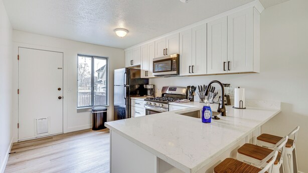 A modern kitchen with white cabinetry, a central island, stainless steel appliances, and a window providing natural light. - Salt Lake County Home Near 4 Major Ski Resorts! (Midvale)