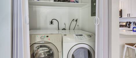 A laundry room with two front-loading washing machines and a shelf above them.