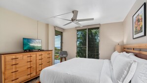 Um quarto com cama, cômoda de madeira, ventoinha no teto, televisão e janela com persianas.
