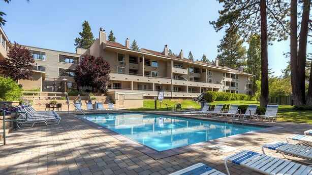 Zona de piscina con sillones reclinables y un edificio con varios balcones al fondo.