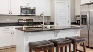 A modern kitchen with white cabinets, stainless steel appliances, a granite countertop, and a central island with stools. - Red Cliffs Getaway 3 Bedroom Townhouse (Washington)