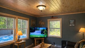 Ein gemütliches Wohnzimmer mit Kamin, Fernseher und Blick auf eine Whirlwanne im Freien.