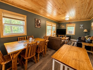 L’intérieur d’une cabane comprend une table à manger, des chaises, un canapé, un téléviseur et une cheminée.
