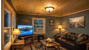 Ein gemütliches Wohnzimmer mit Fernseher, Kamin, Ledersofa und rustikaler Einrichtung.