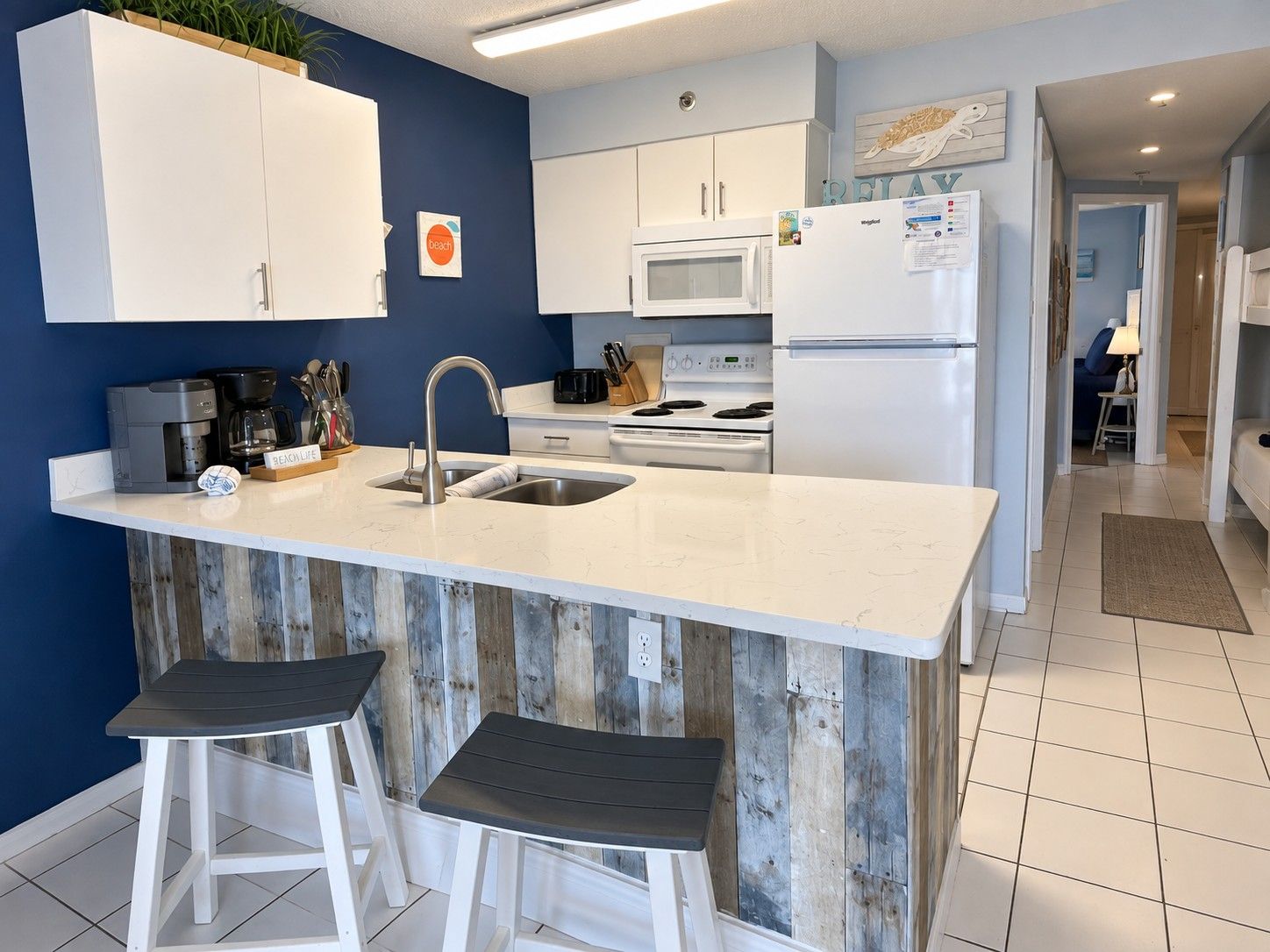 Una cocina moderna con armarios blancos, una isla central con taburetes, un microondas y un refrigerador.