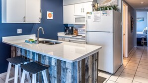 Une cuisine moderne avec des meubles blancs, un grand îlot central doté de tabourets, un réfrigérateur et un four à micro-ondes.