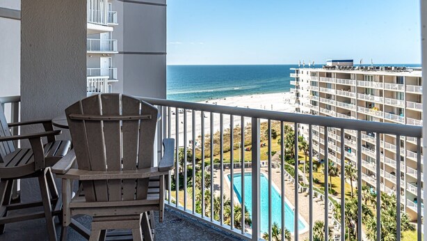 Un balcon avec des chaises, une piscine et une vue sur la plage et l’océan.