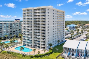 A multi-story hotel with a swimming pool, outdoor seating, and a parking area. - Tradewinds 908 | Heated Swim-Through Pool | Gulf Views | Orange Beach (Orange Beach)