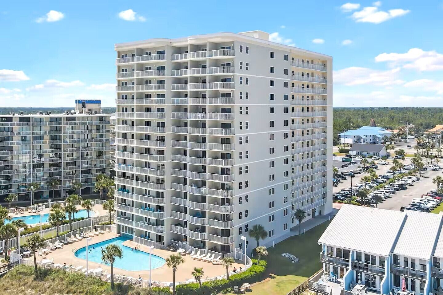 A multi-story hotel with balconies, a swimming pool, and a parking lot.