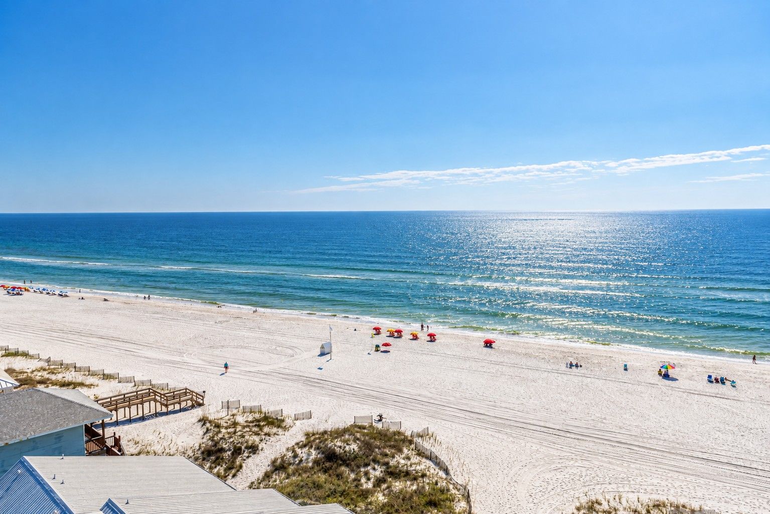 A beach with a wooden walkway, beach umbrellas, and a clear view of the ocean.