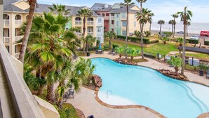 A resort with a large swimming pool surrounded by palm trees and a view of the ocean. - Ocean & Pool Views, W/D in Condo, 2 King Beds (Galveston)