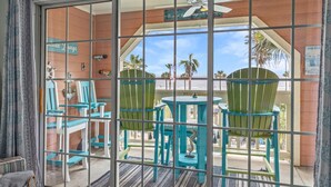 A room with a large window, a ceiling fan, and a view of palm trees. - Ocean & Pool Views, W/D in Condo, 2 King Beds (Galveston)