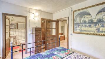 Een slaapkamer met een bed, een houten garderobe, een spiegel en een ingelijst schilderij aan de muur.