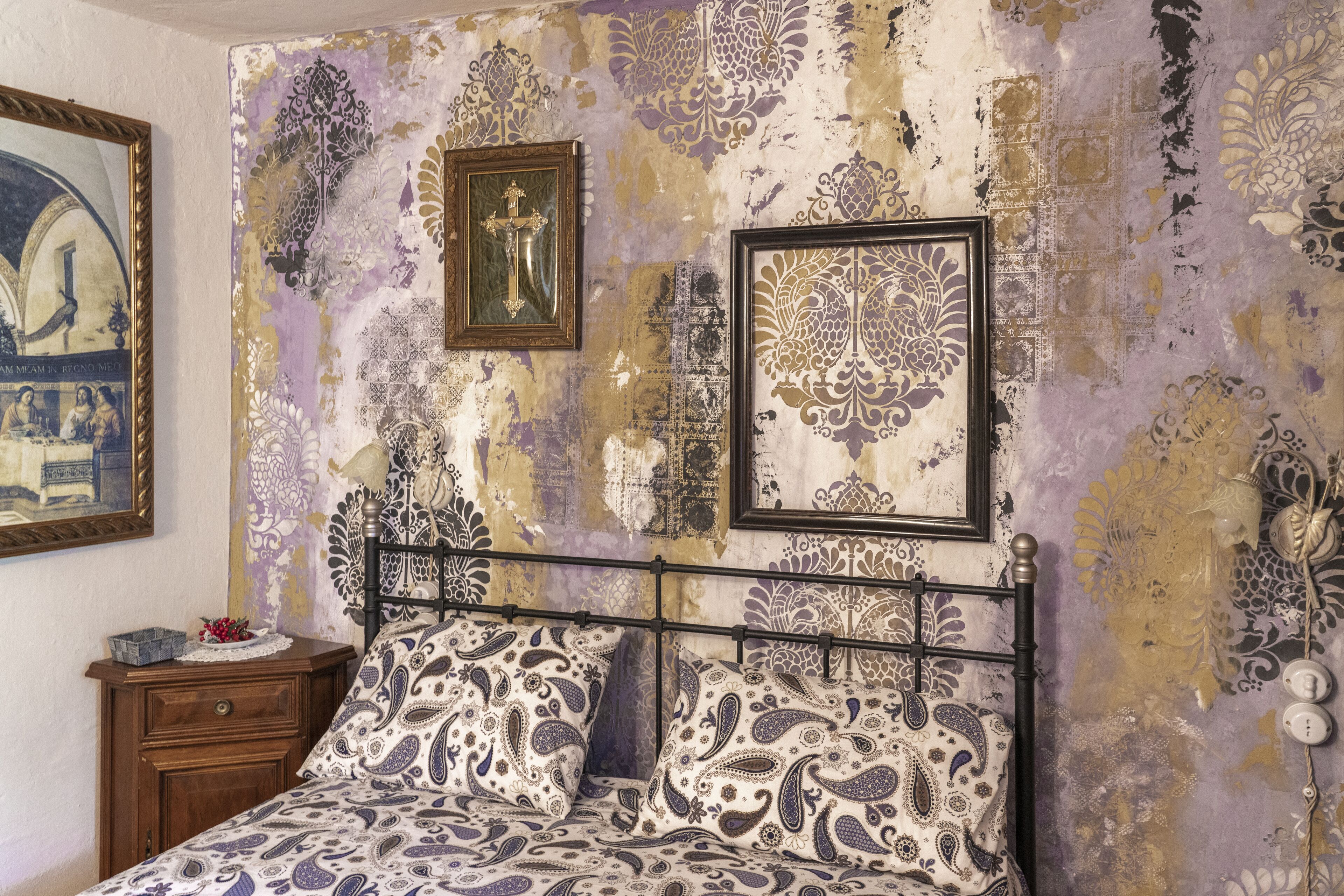 Un dormitorio con cama, mesita de noche y pared decorada con motivos y cuadros.