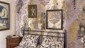 Un dormitorio con cama, mesita de noche y pared decorada con motivos y cuadros.