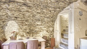A rustic stone interior with a dining table and chairs, a staircase, and a small cabinet.