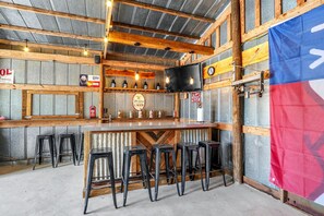 Un espace bar avec des poutres en bois, un comptoir et des tabourets. On y trouve des tireuses à bière et un téléviseur fixé au mur.