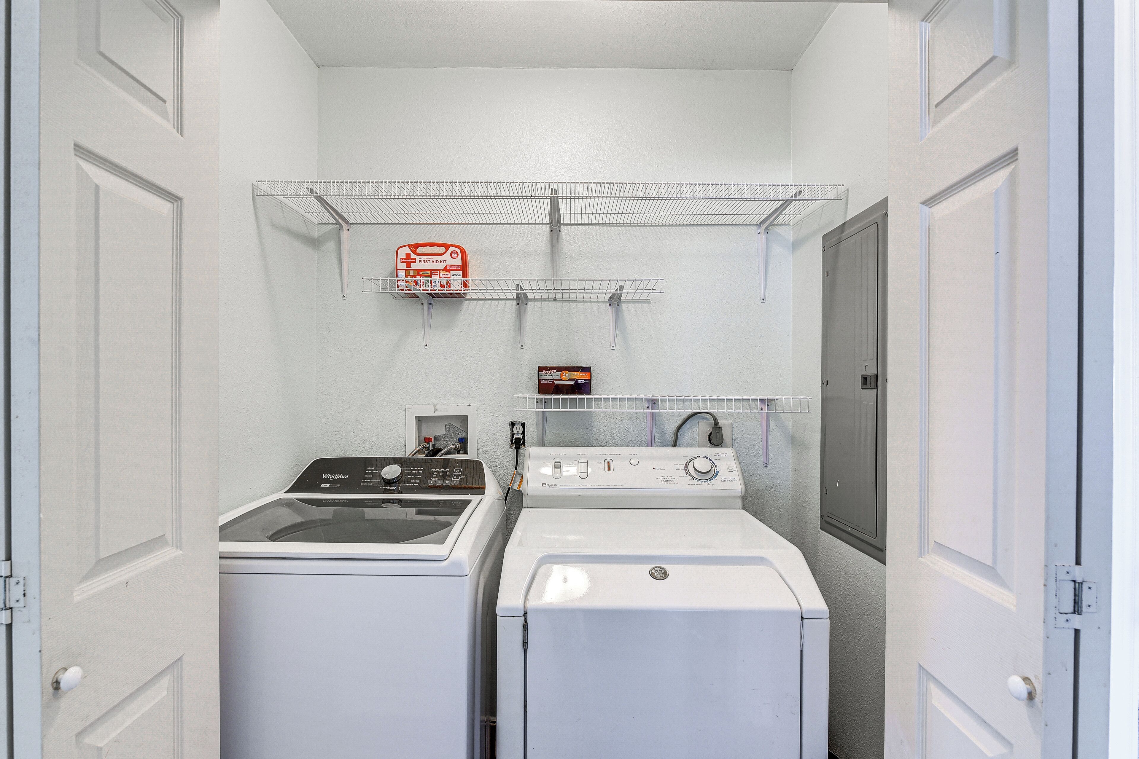 A laundry room with two washers and dryers, a metal shelf with a fire extinguisher, and a small storage cabinet.