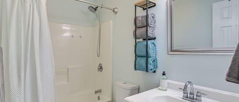 Un baño con ducha, inodoro, lavamanos y un perchero con toallas dobladas.