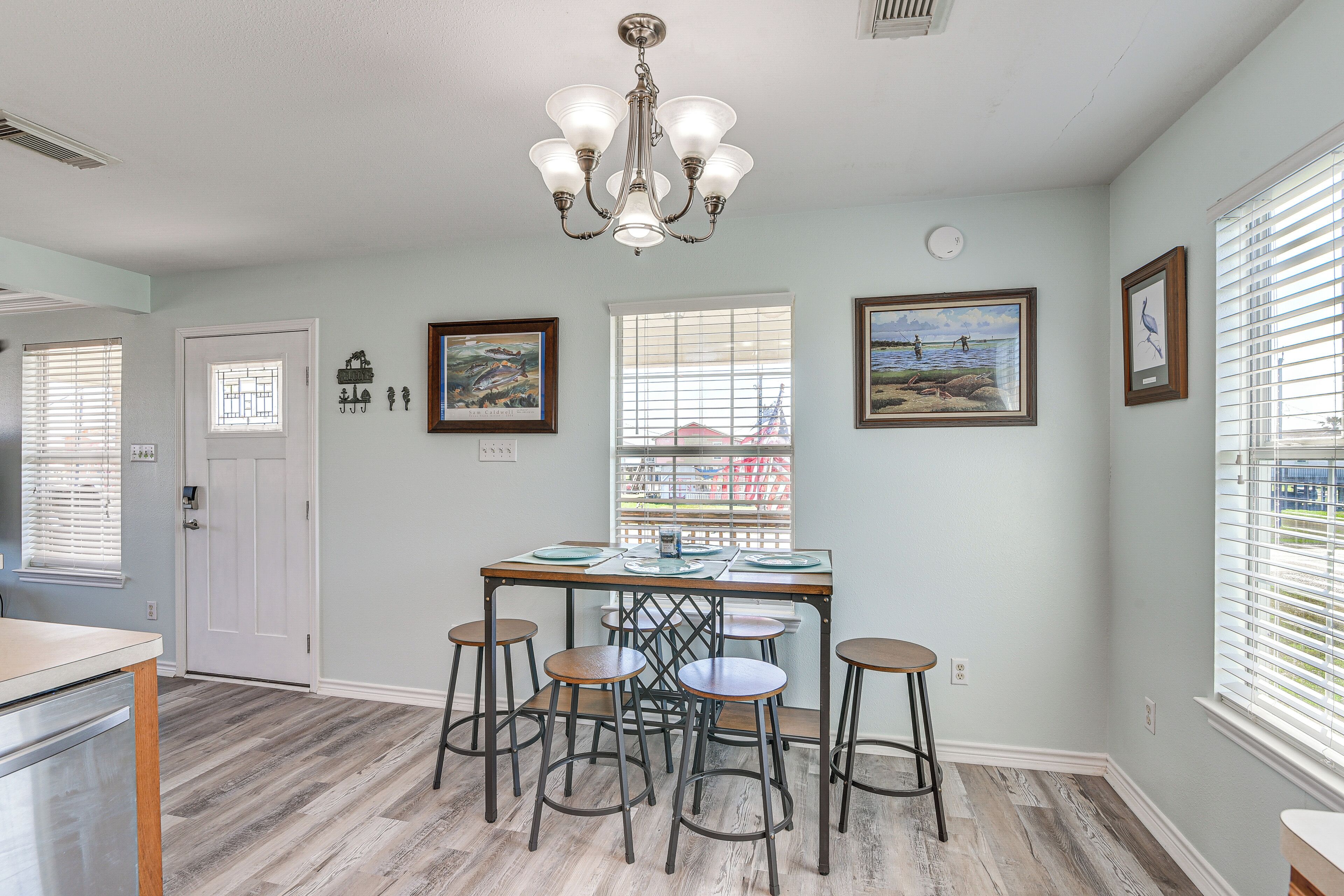 A dining area with a table and four stools, a chandelier, and two framed pictures on the wall.