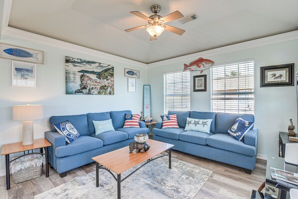 A living room with a blue sofa set, a wooden coffee table, and a ceiling fan. - Walk to Shore: Surfside Beach Home w/ Balcony! (Freeport)