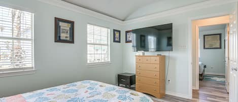 A bedroom with a bed, dresser, TV, and framed pictures on the wall.
