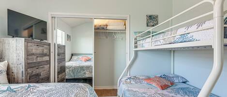A bedroom with bunk beds, a TV on a wooden dresser, and a walk-in closet.