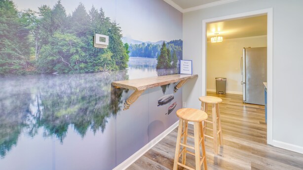 A kitchen with a wooden bar counter, two stools, and a wall mural of a lake surrounded by trees.