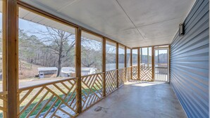 A covered porch with large windows, a wooden railing, and a view of a lake and trees.