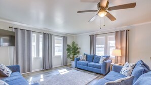 A living room with a blue sofa set, a white rug, a ceiling fan, and a potted plant.