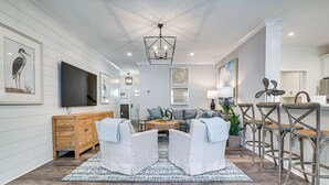 A modern living room with a large flat-screen TV, a wooden cabinet, a white sofa set, a patterned rug, and a bar area with stools. - Idyllic Murrells Inlet Home < 1 Mi to Marsh Walk (Murrells Inlet)