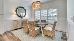A dining area with a round table, wicker chairs, a chandelier, a mirror, and a window with blinds. - Idyllic Murrells Inlet Home < 1 Mi to Marsh Walk (Murrells Inlet)