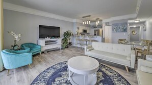 Een moderne woonkamer met een flatscreen televisie, blauwgroene fauteuils, een witte bank en een ronde salontafel.