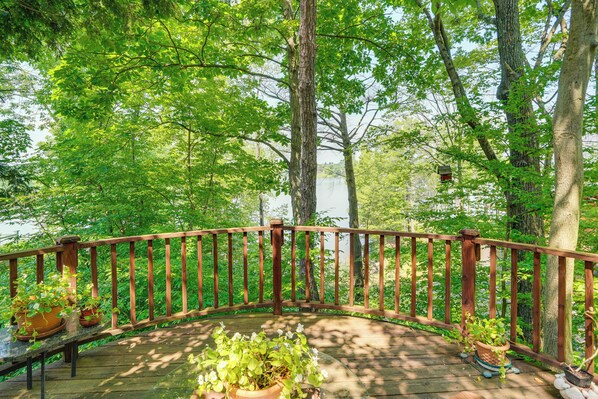 A wooden deck with potted plants, surrounded by trees and a lake view.