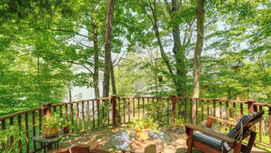 A wooden deck with a glass table surrounded by chairs, potted plants, and a view of a forested area. - Treehouse Sanctuary Nature Retreat (Athens)