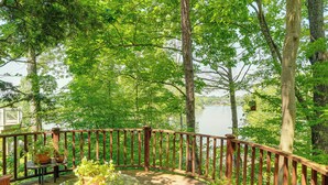 A wooden deck with a glass table and chairs, surrounded by a wooden railing, overlooking a lake. - Treehouse Sanctuary Nature Retreat (Athens)